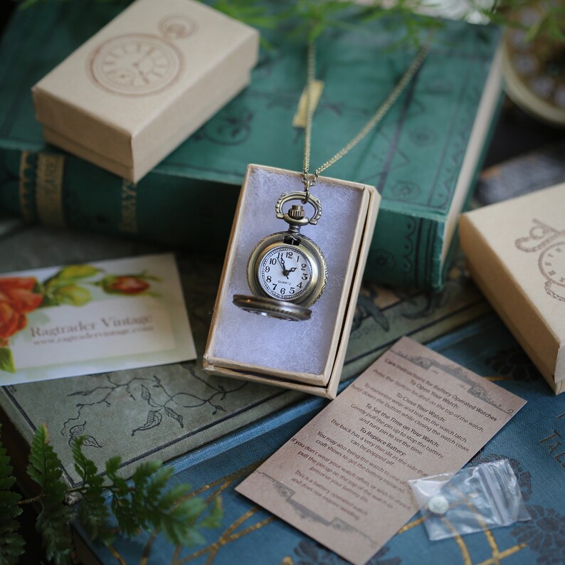 Brass pocket watch displayed in a box. Watch is open so that the face is visible. The face is white with black numbers.