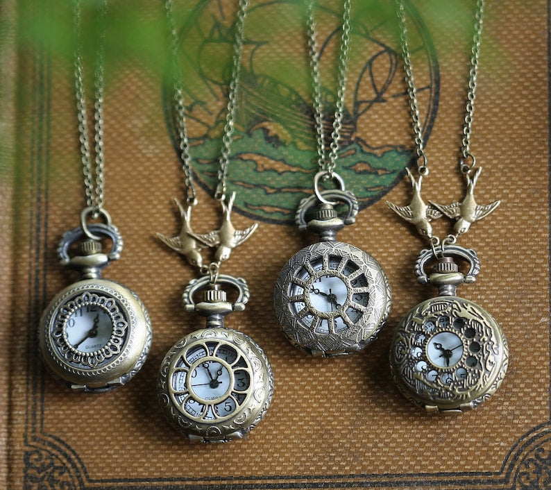 A collection of vintage-style pocket watch necklaces. Lace Circlet, Daisy Window, Sun Window, and Sun and Moon styles. These watches are displaying both simple chains and chains with birds.