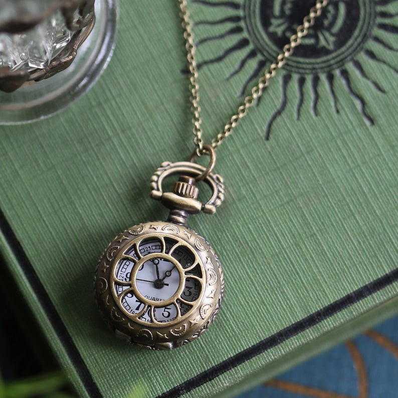 Antiqued brass pocket watch with a Daisy Window design. This watch is attached to a simple brass chain.