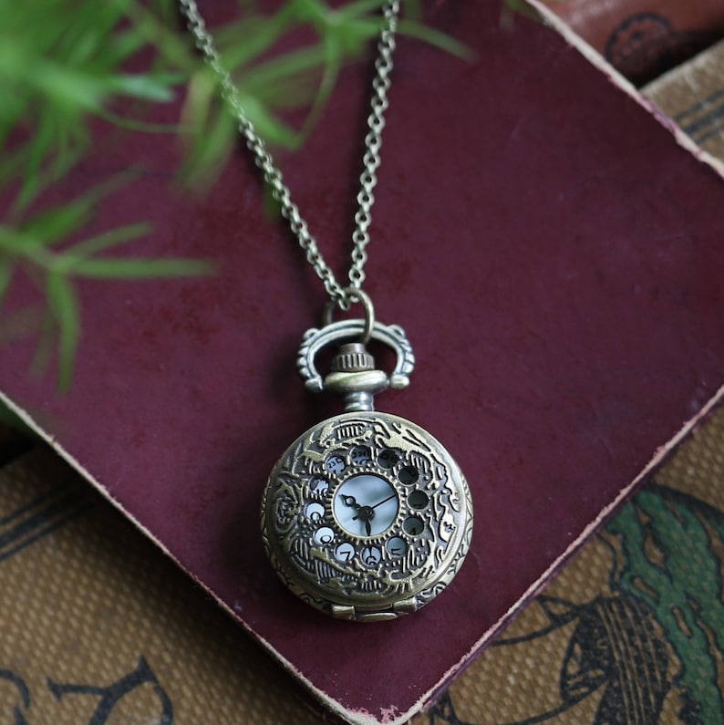 Antiqued brass pocket watch with a Sun and Moons design. This watch is attached to birds connected to a brass chain.