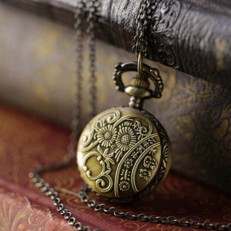Antiqued brass pocket watch displaying the watch's back. The back features an intricate floral design.