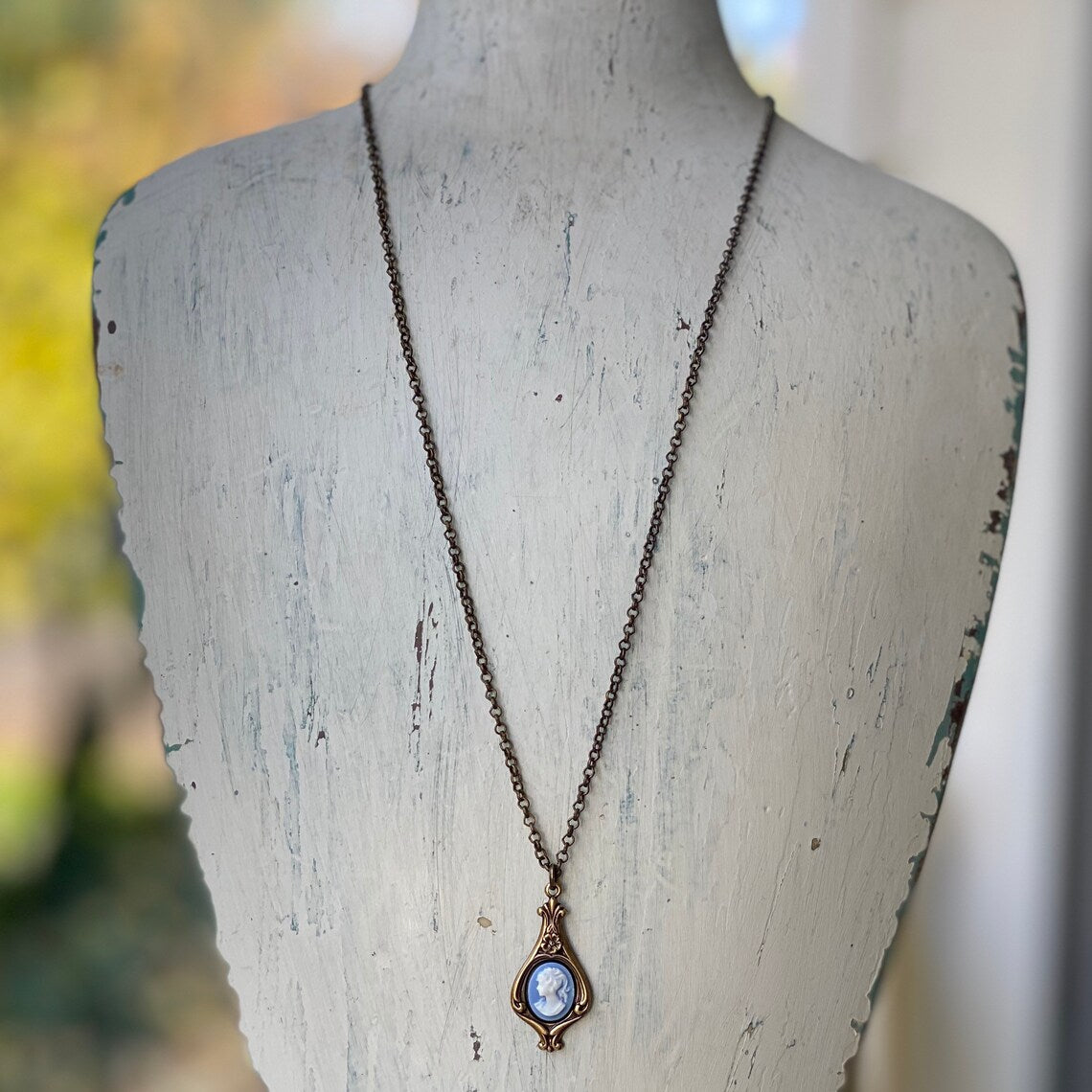 Antiqued brass necklace with a blue and white cameo of a woman on a filigree garden drop setting.