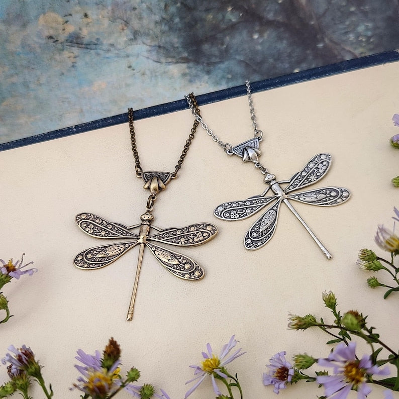 Antiqued silver and brass dragonfly pendants with ornate art deco connecters side-by-side.