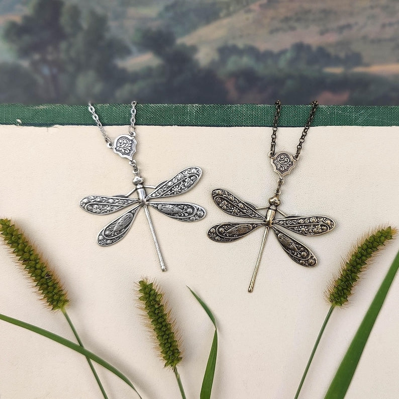 Antiqued silver and brass dragonfly pendants with ornate flourish connecters side-by-side.