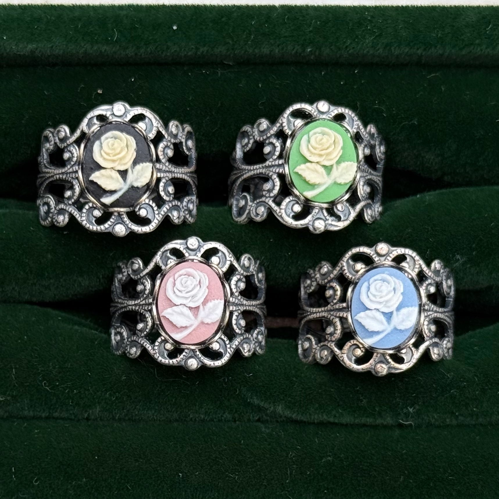 Four antiqued silver filigree rings with rose cameos. The cameos have a white flower with different colored backgrounds: black, green, pink, and blue