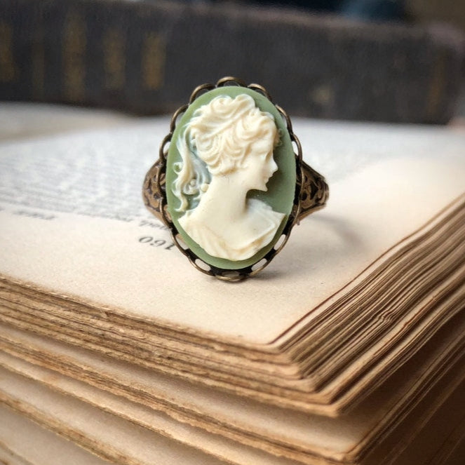 A vintage style cameo ring with a white lady on a green background. This oval cameo is set on an adjustable brass oakleaf band.