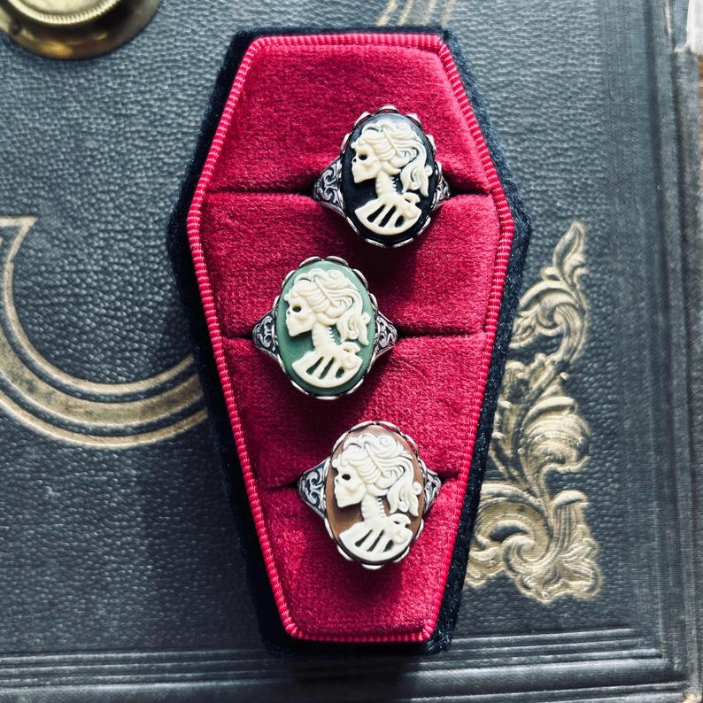 Three cameo rings with white skeleton ladies on black, green, and brown backgrounds.
