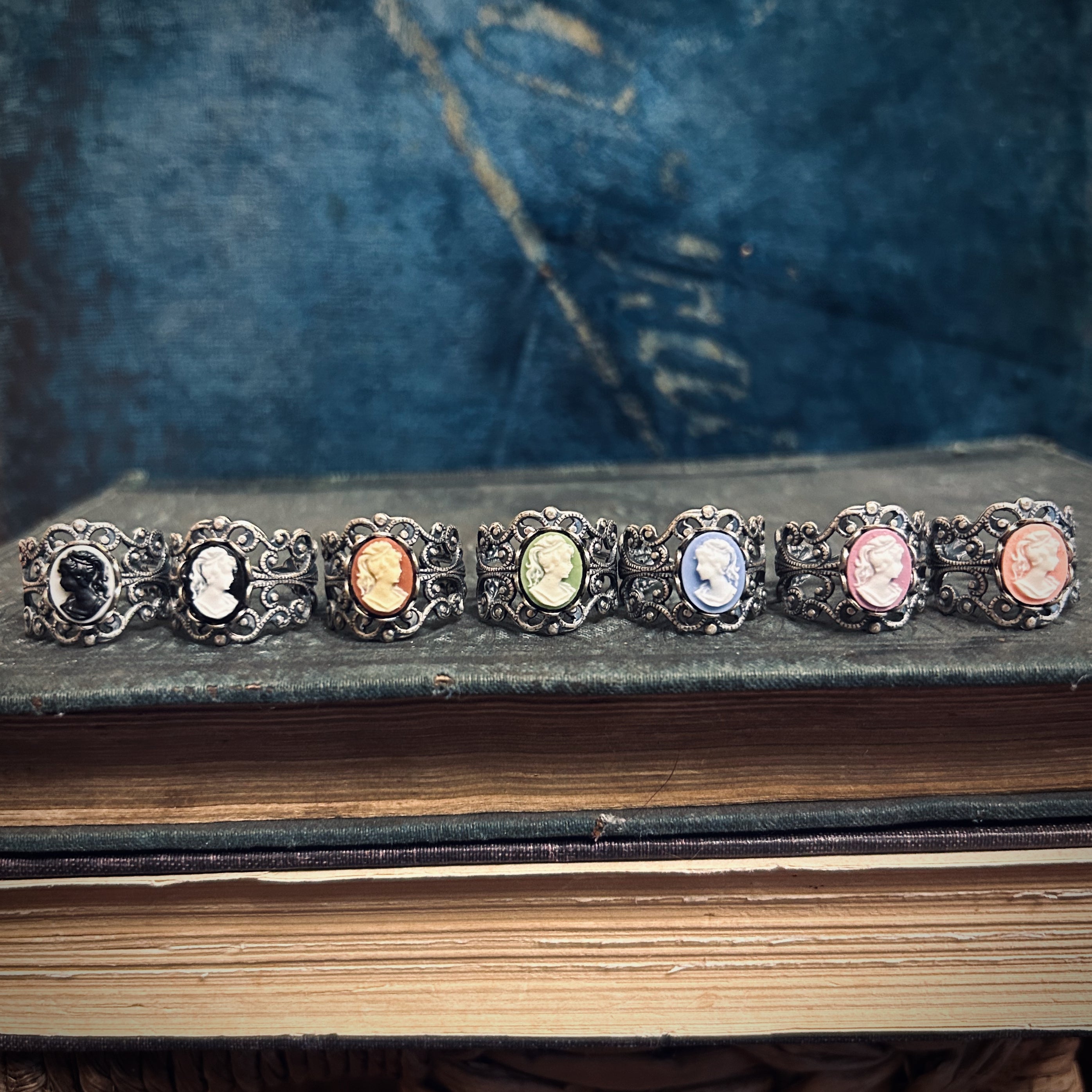 Seven silver adjustable filigree cameo rings with different colored profile cameos. The options are a black profile on white, white on black, cream on orange, white on green, white on blue, white on pink, and cream on peach.