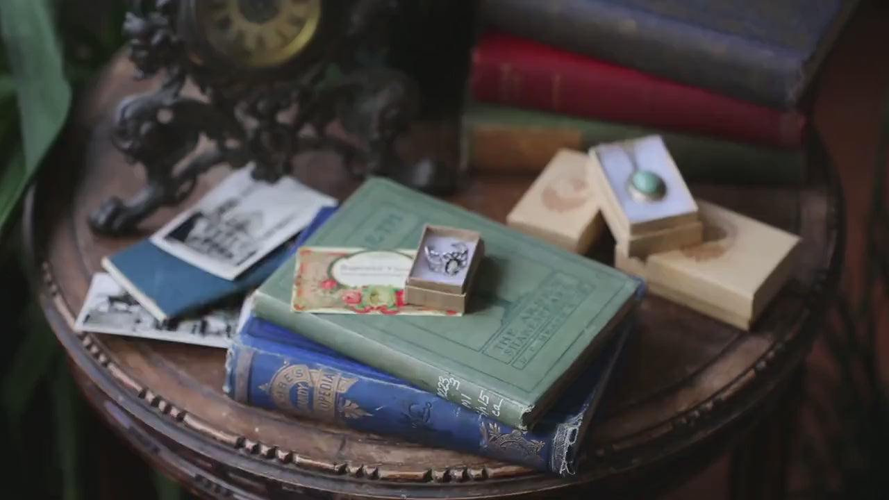 Video of a model adjusting and putting on an antiqued silver filigree ring with a rose cameo.
