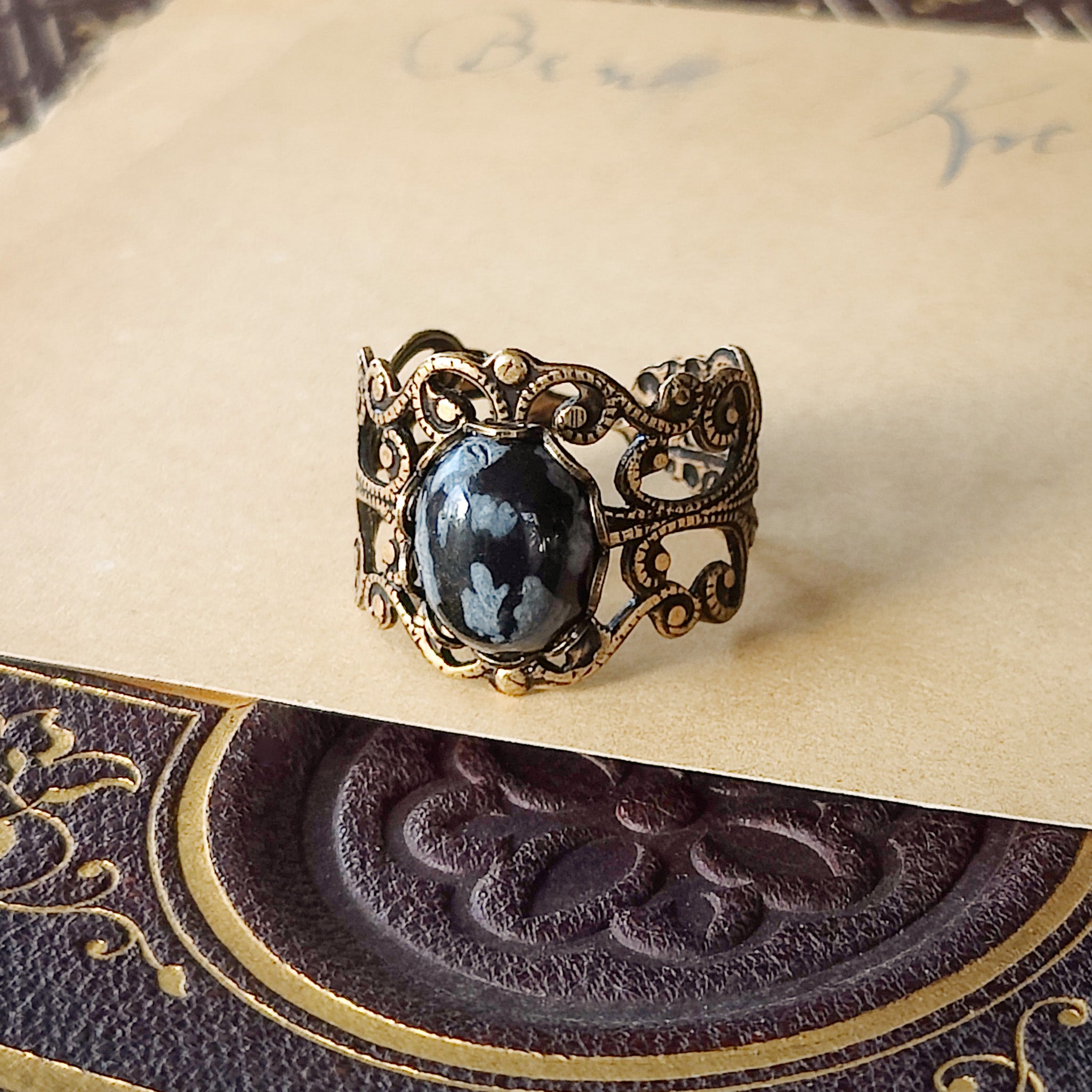 rich antiqued brass modern vintage inspired adjustable filigree ring with a dark black and gray mottled snowflake obsidian oval semi-precious mineral stone set in a military aesthetic