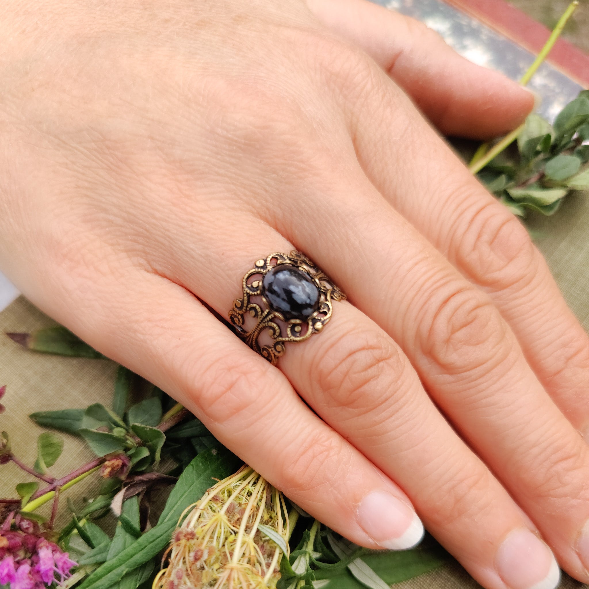 rich antiqued brass modern vintage inspired adjustable filigree ring with a dark black and gray mottled snowflake obsidian oval semi-precious mineral stone set in a hippie goth aesthetic