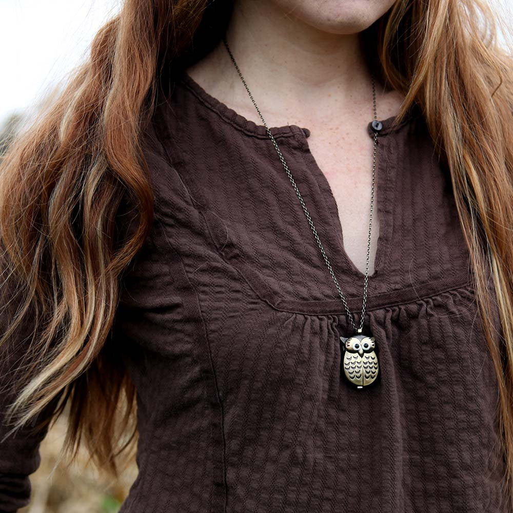 A bronze owl-shaped watch necklace with a quartz face. This watch is displayed closed, with the owl's wings closed to cover the watch face. Watch is displayed on a model.