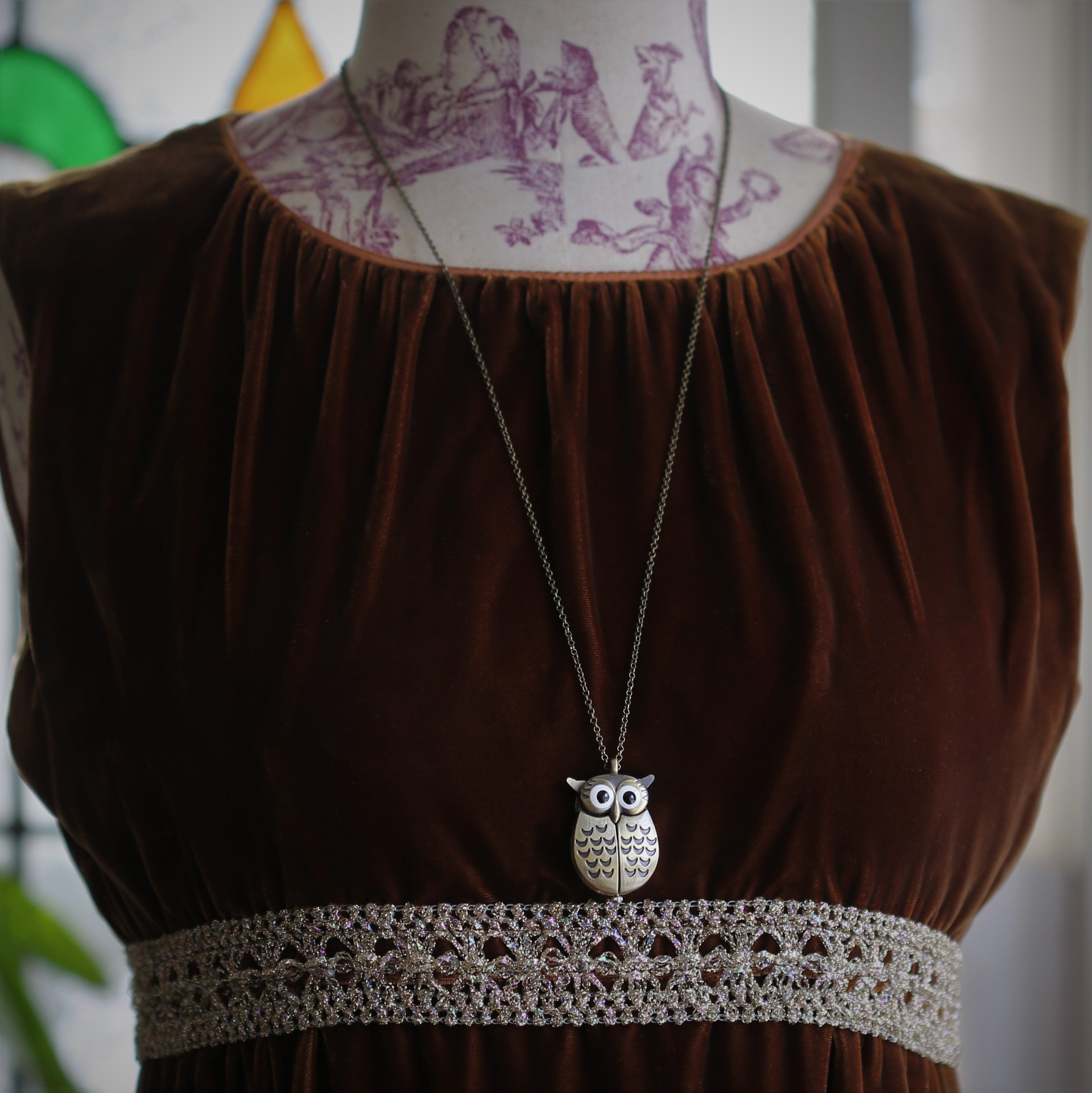 A bronze owl-shaped watch necklace with a quartz face. This watch is displayed on a display bust.