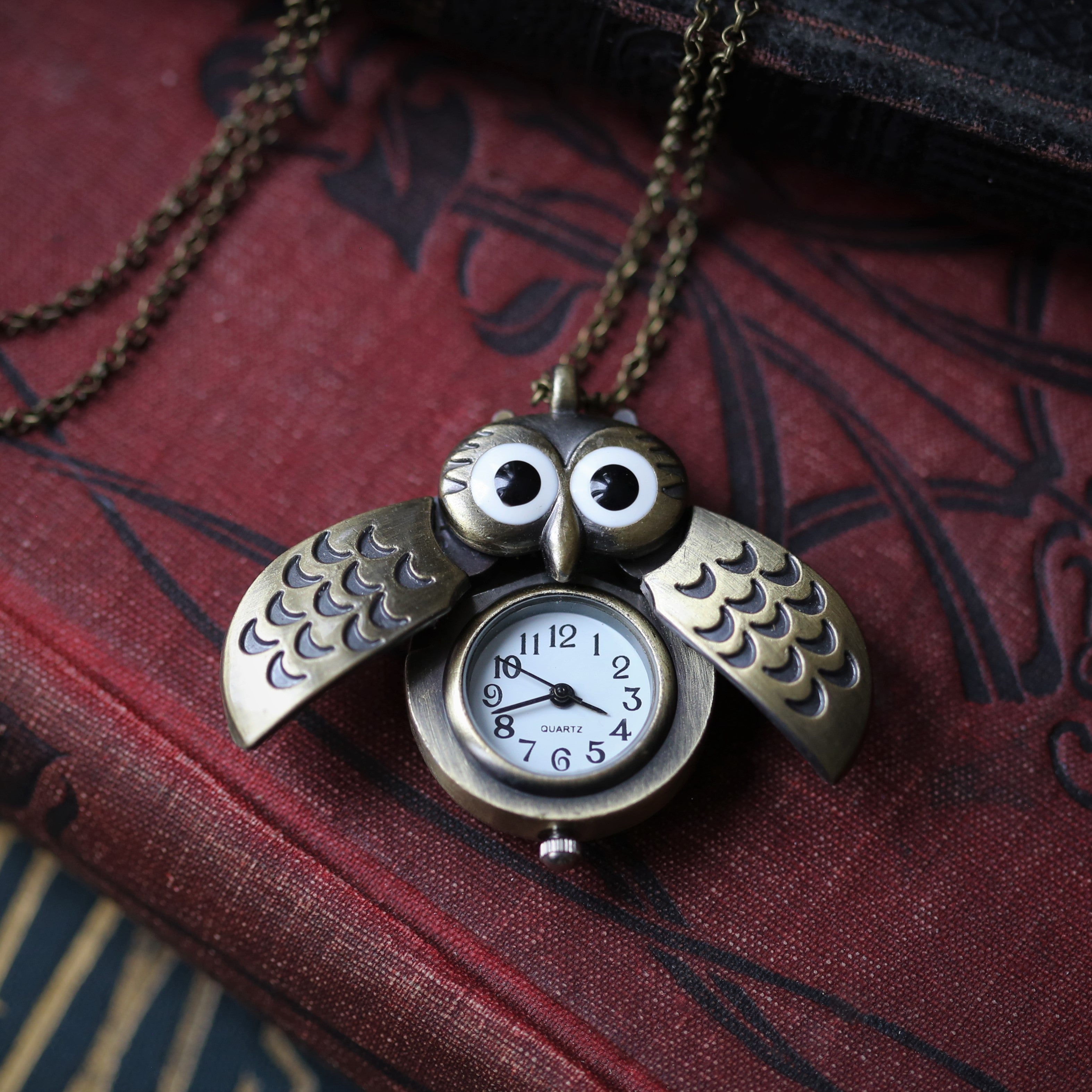 A bronze owl-shaped watch necklace with a quartz face. This watch is displayed open, with the owl's wings open to show the watch face.