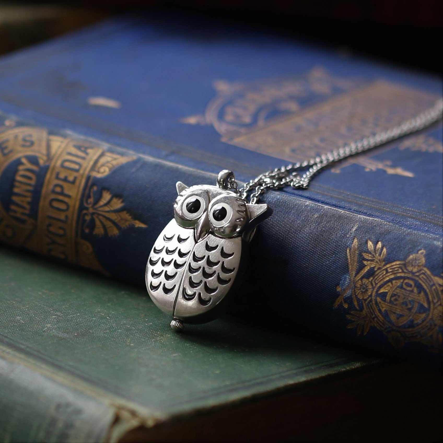 A silver owl-shaped watch necklace. This watch is closed with the owl's wings covering the watch face.