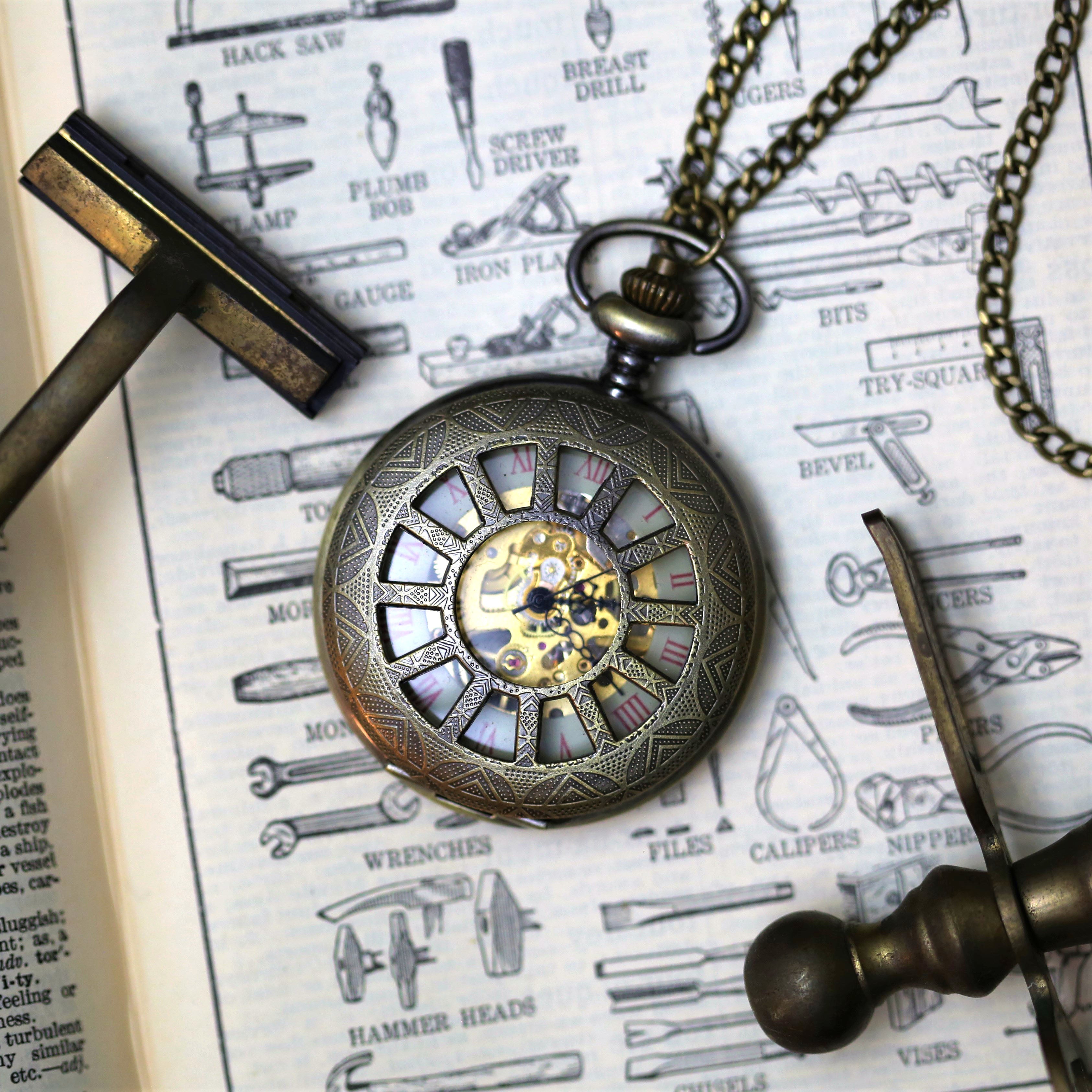 Antiqued brass mechanical pocket watch with a cogwheel design on the front. The watch is closed, but internal gears and numerals are visible through the lid.