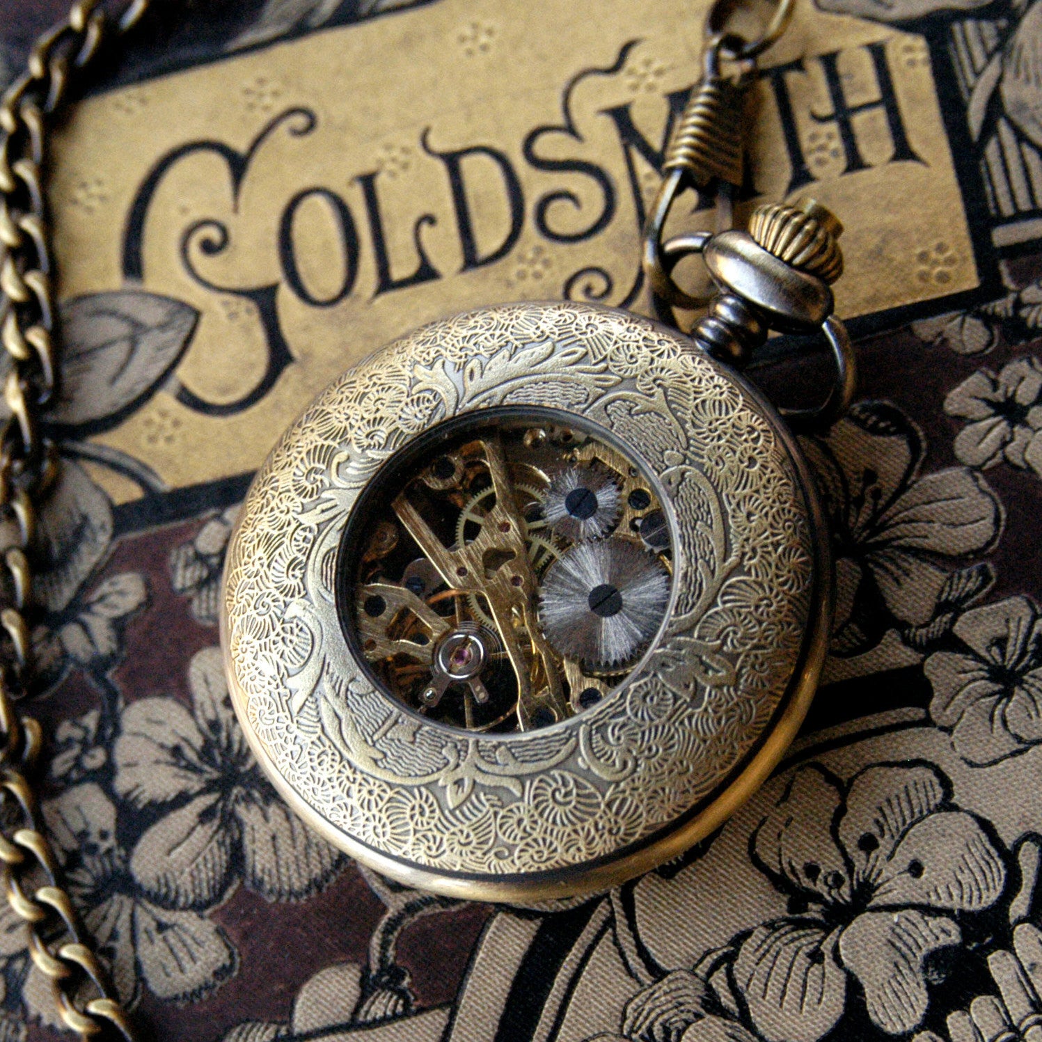 Antiqued brass Cogwheel mechanical pocket watch face down to display an ornate back panel with a window to internal gears in the center.