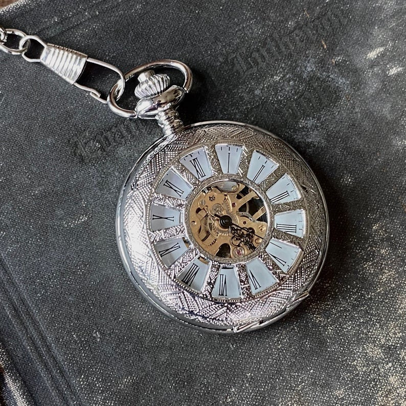 Silver mechanical pocket watch with a cogwheel design on the front, attached to a silver watch chain. The watch is closed, but internal gears are visible through the lid.