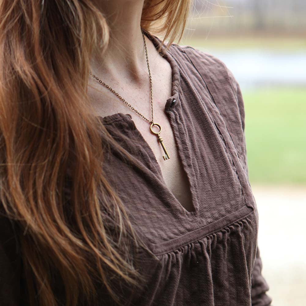 Simple brass key with an oval head on a necklace chain.