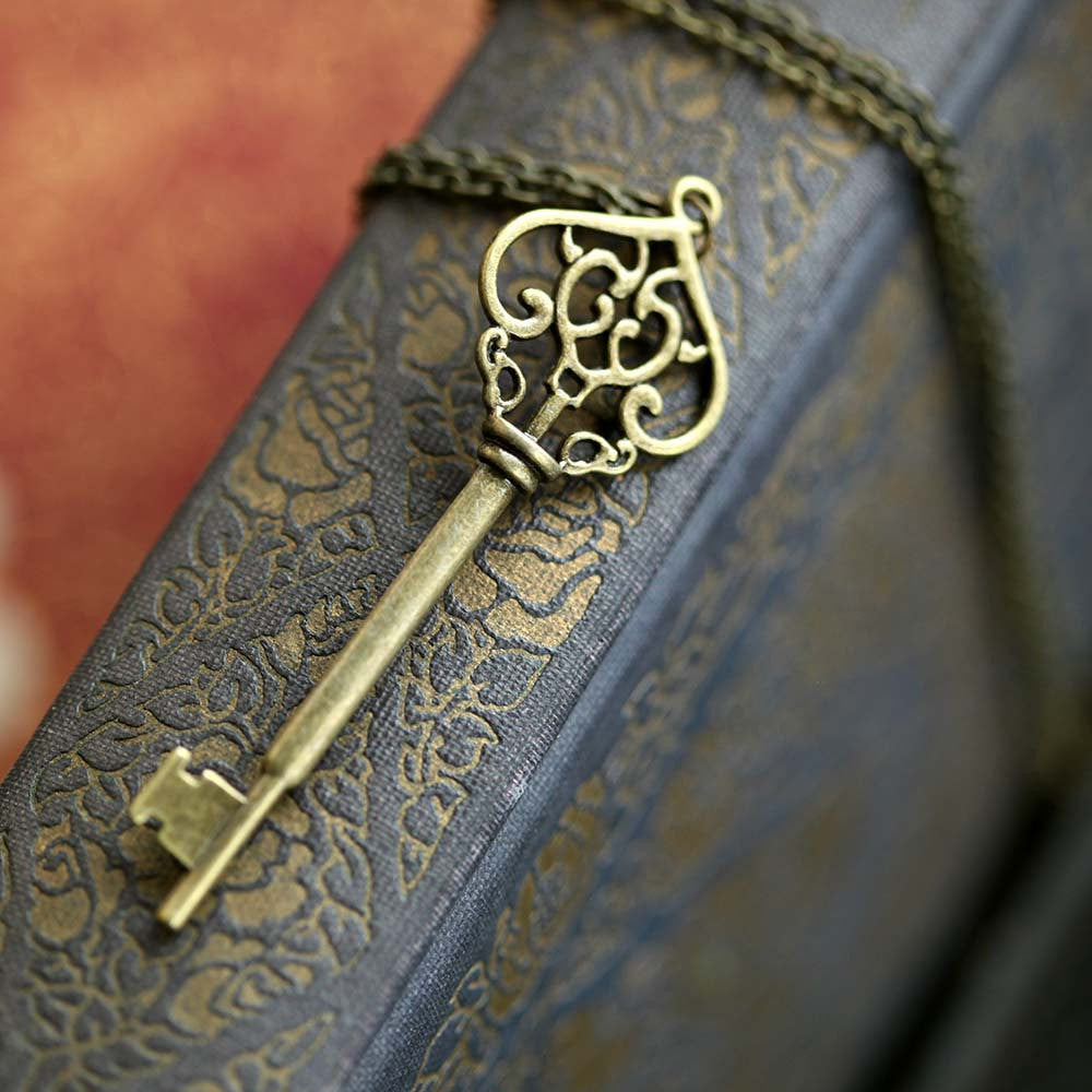 Antiqued brass key pendant necklace. The head of the key is shaped like an ornate upside down heart with two 'c's facing each other inside.