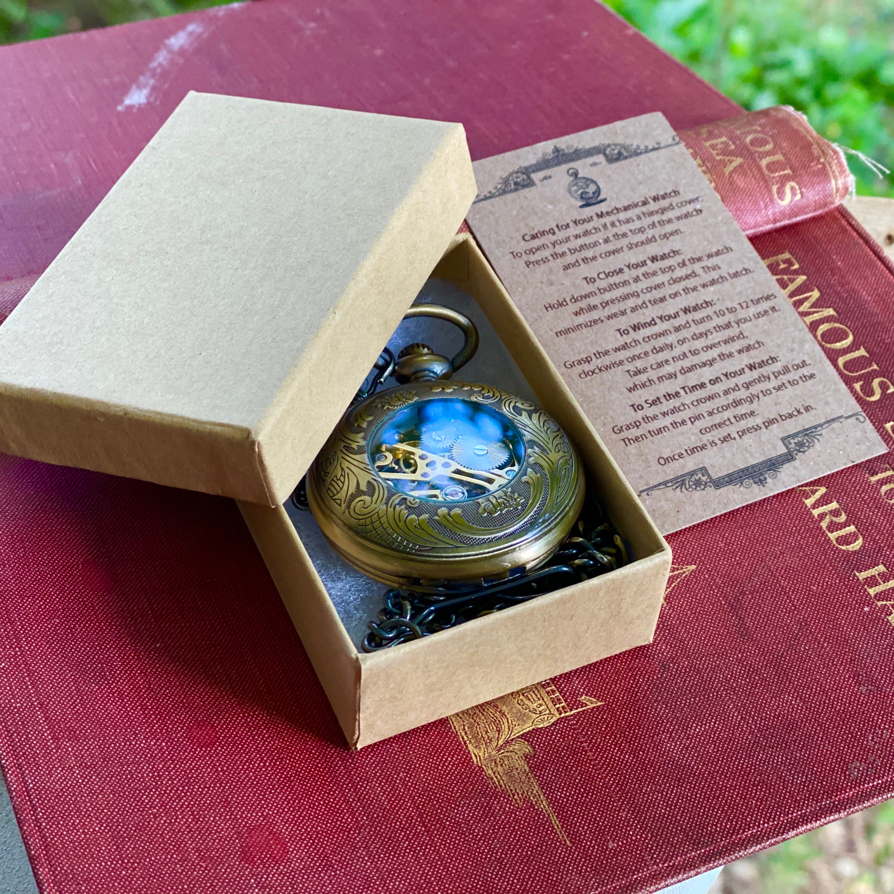 Antiqued brass mechanical pocket watch with zodiac symbols around the lid displayed in a box.