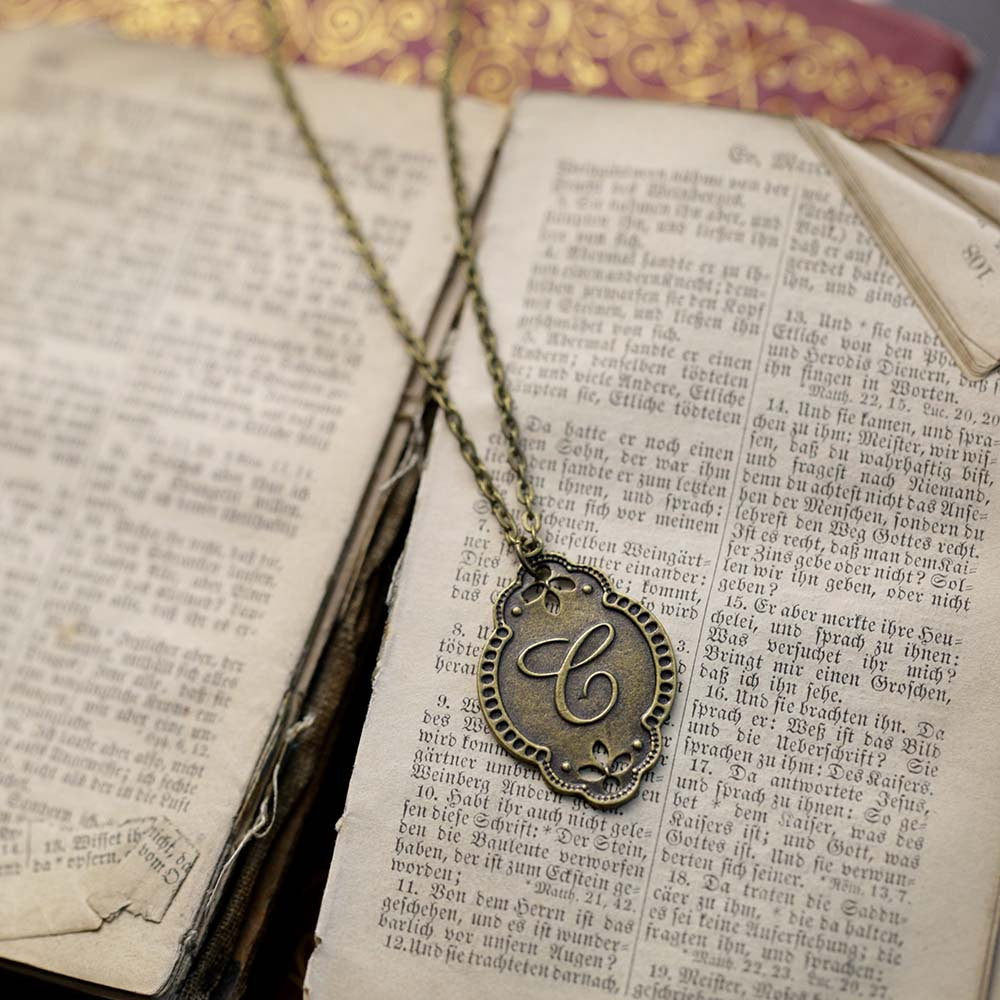 Antiqued brass letter 'C' pendant with an ornate border. The pendant is roughly oval shaped.