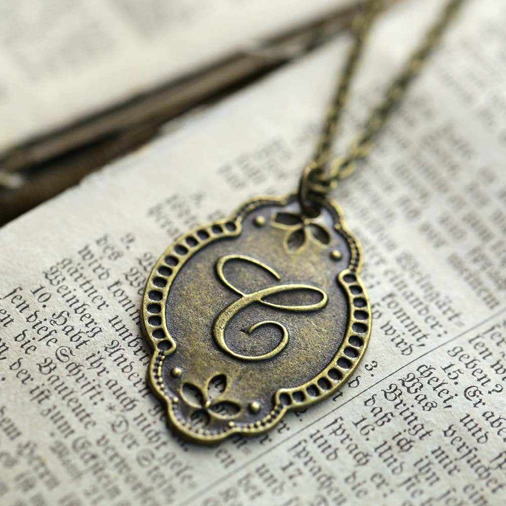 Antiqued brass letter 'C' pendant with an ornate border. The pendant is roughly oval shaped.