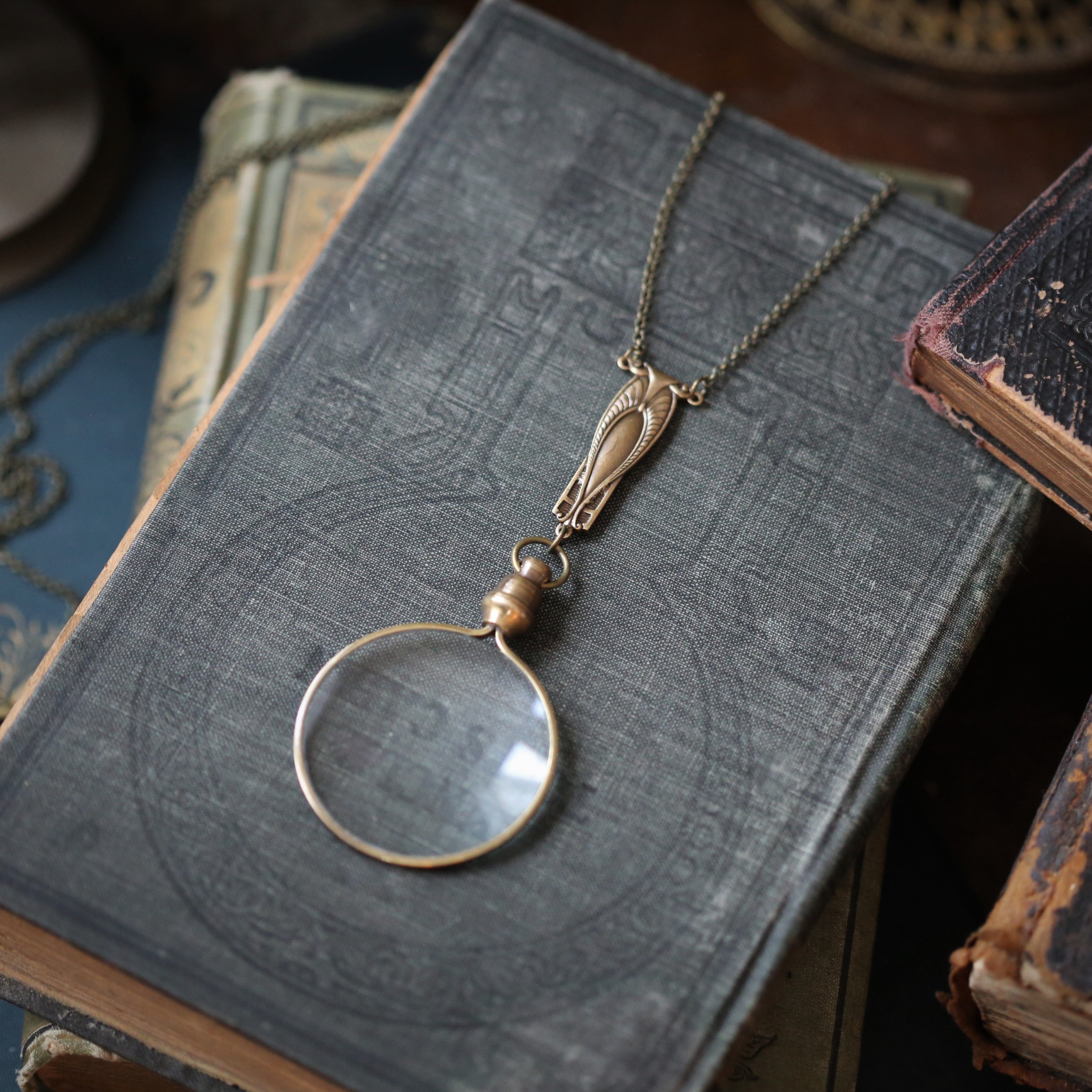 Antiqued brass round-lens glass magnifying glass attached to an art deco connector and a necklace chain.