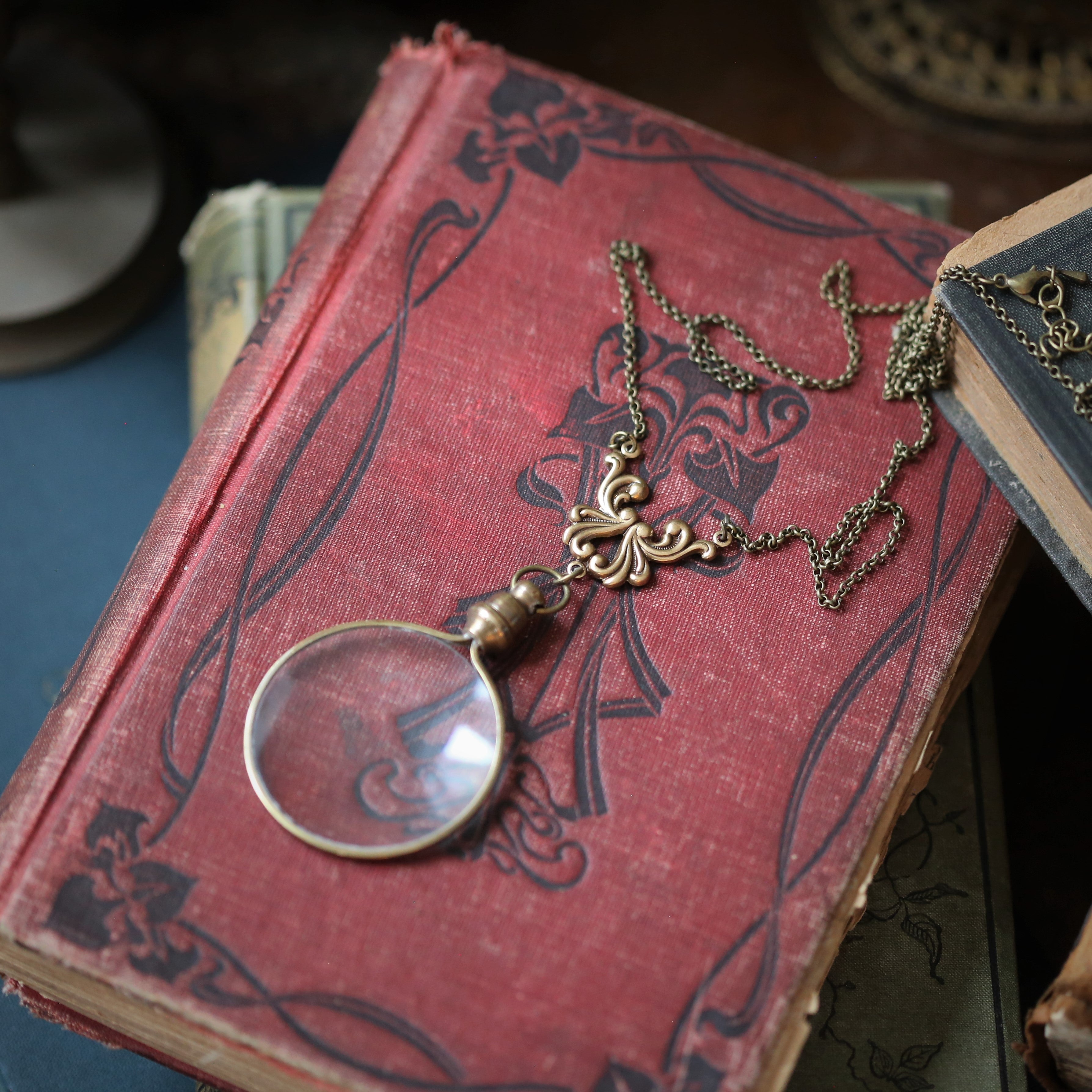 Antiqued brass round-lens glass magnifying glass attached to a swan wing connector and a necklace chain.