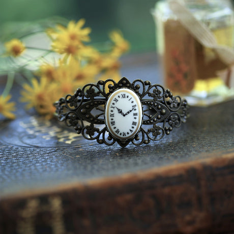 Adjustable antiqued brass filigree cuff bracelet with a vintage style clock face cameo set in a bezel on the front of the bracelet.