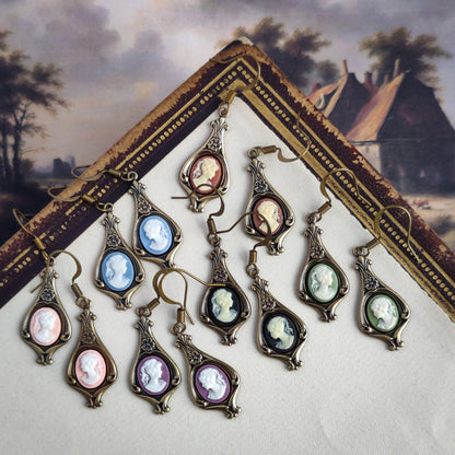 Color options for lady cameo drop earrings. Cream lady on orange,  white lady on green, white on light blue, white on pink, white on black, and white on purple. These options are on brass garden drop earring settings.