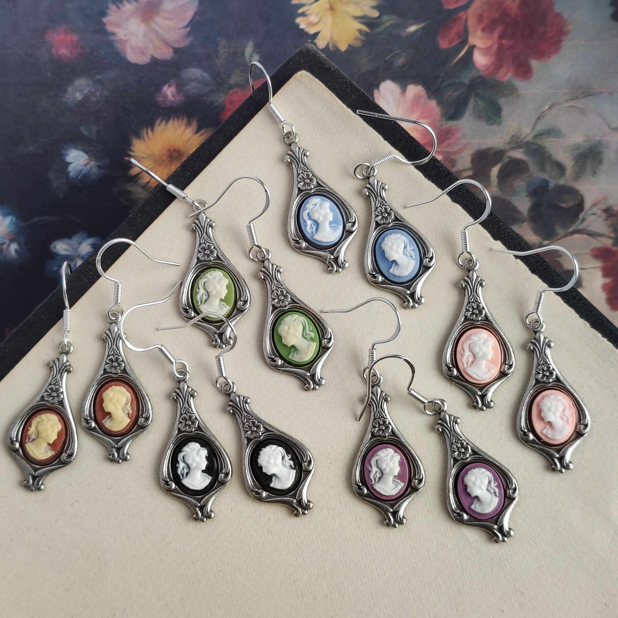 Color options for lady cameo drop earrings. Cream lady on orange,  white lady on green, white on light blue, white on pink, white on black, and white on purple. These options are on silver garden drop earring settings.