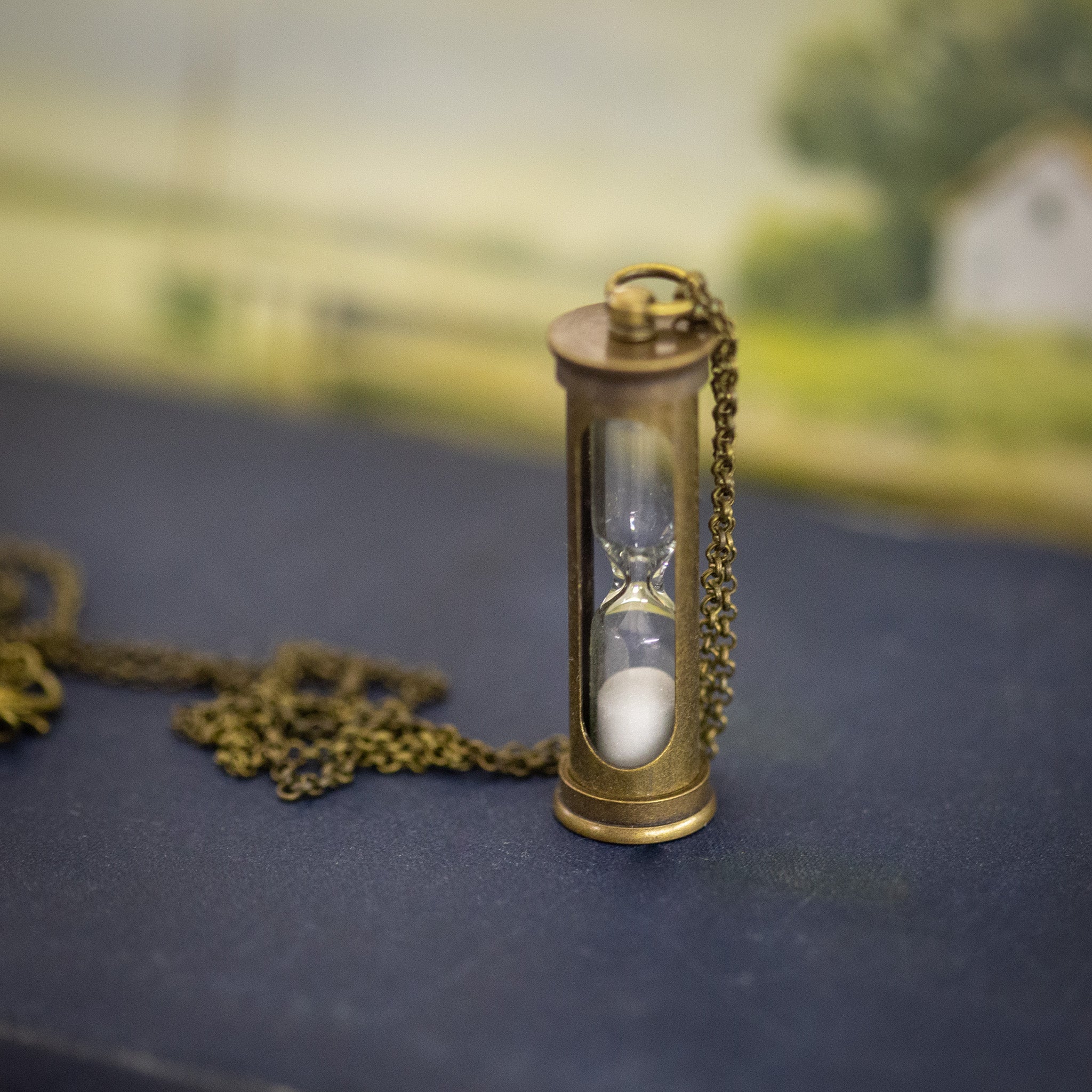A functional hourglass in an antiqued brass frame hanging from a brass chain.