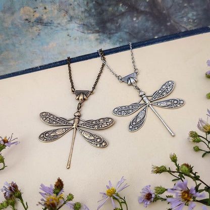 Antiqued silver and brass dragonfly pendants with ornate art deco connecters side-by-side.