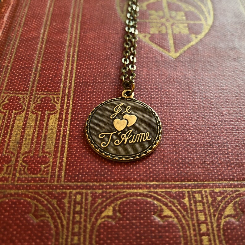 The phrase 'Je T'Aime' and two hearts on a circular brass pendant on a brass chain.