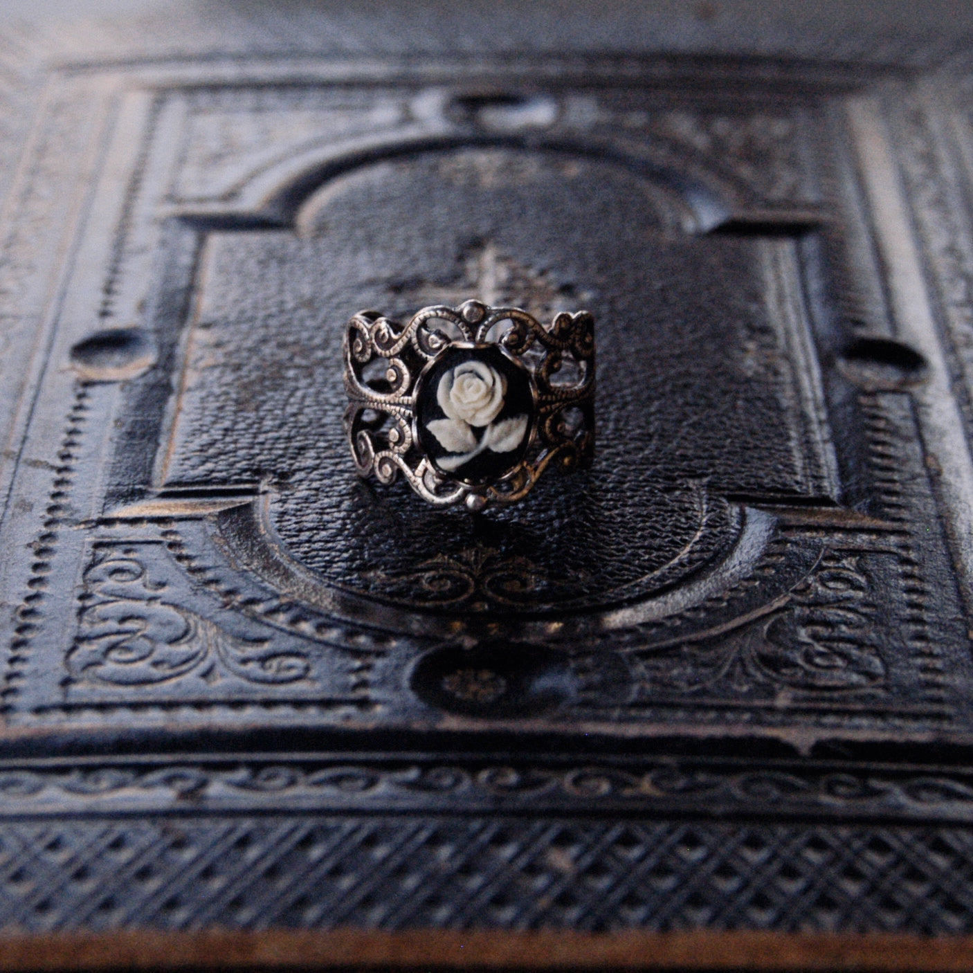 A cameo ring with a white rose on a black background. This oval cameo is set on an adjustable brass filigree ring.