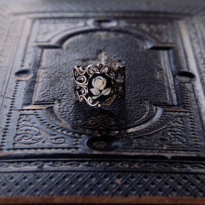 A cameo ring with a white rose on a black background. This oval cameo is set on an adjustable brass filigree ring.