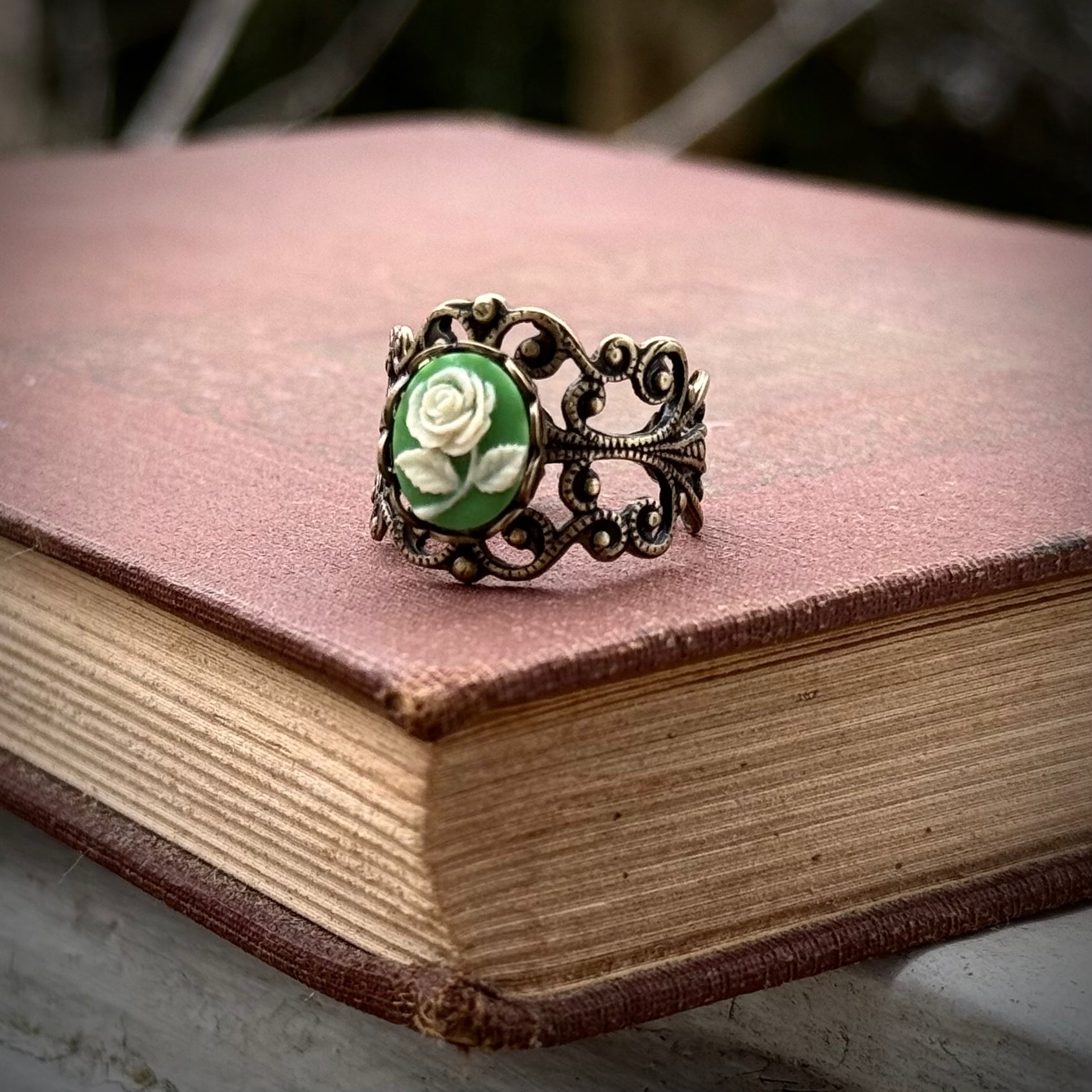 A cameo ring with a white rose on a green background. This oval cameo is set on an adjustable brass filigree ring.