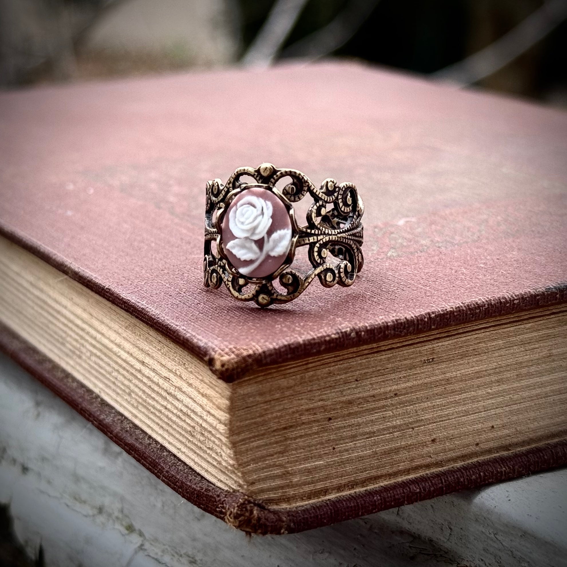 A cameo ring with a white rose on a pink background. This oval cameo is set on an adjustable brass filigree ring.