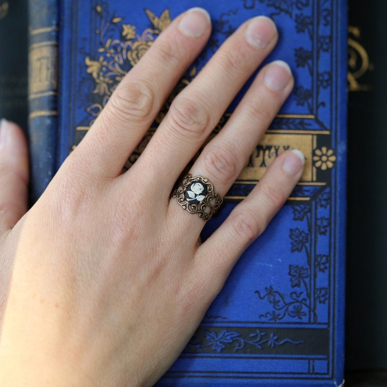 A cameo ring with a white rose on a black background. This oval cameo is set on an adjustable silver filigree ring.