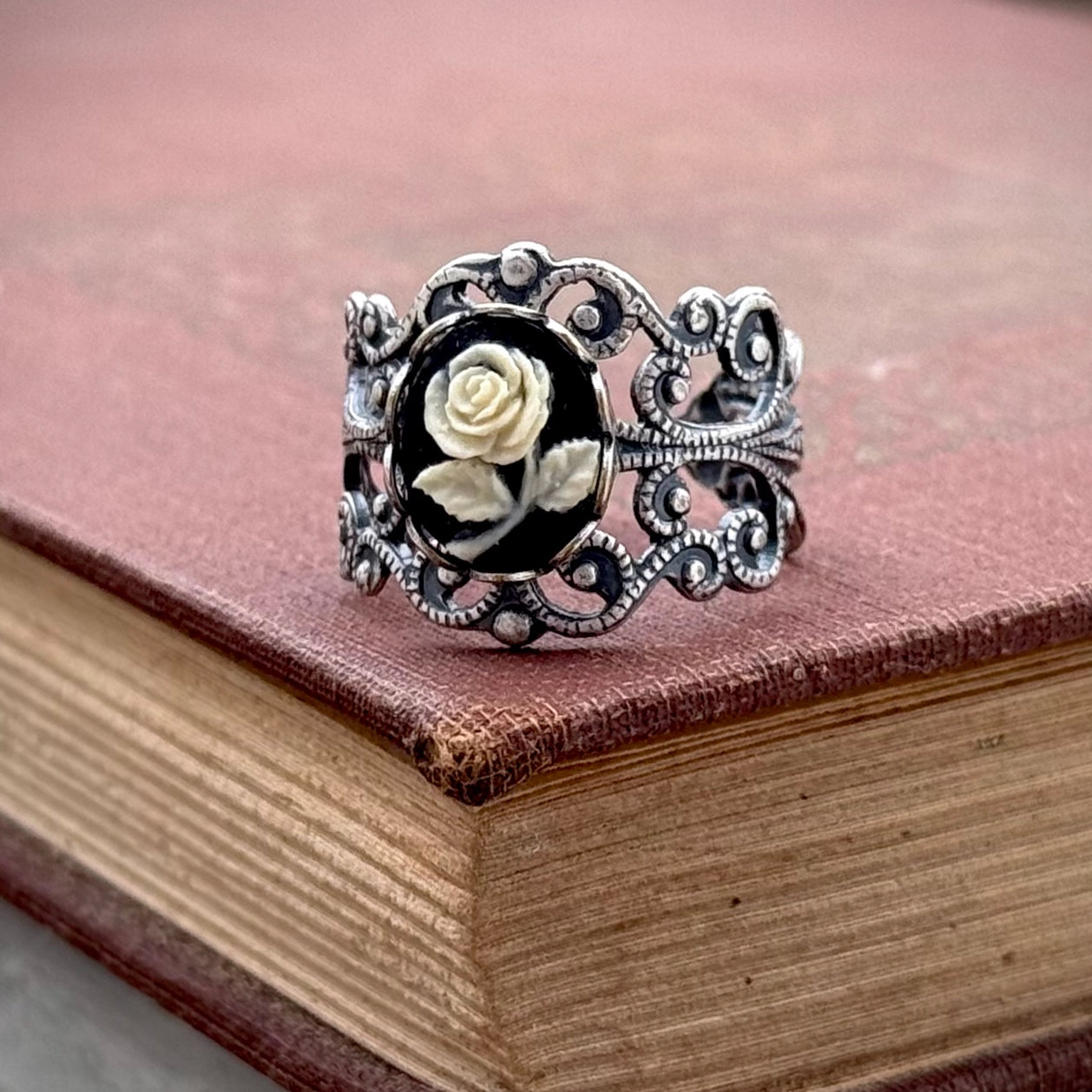 A cameo ring with a white rose on a black background. This oval cameo is set on an adjustable silver filigree ring.