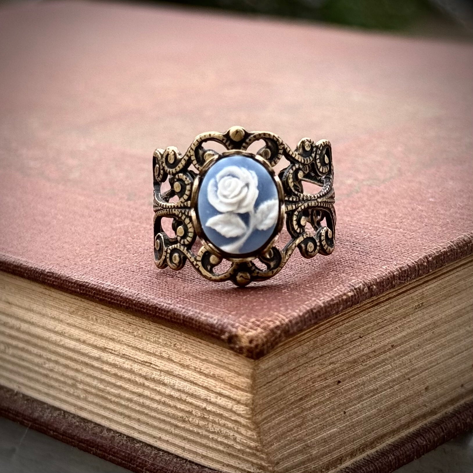 A cameo ring with a white rose on a blue background. This oval cameo is set on an adjustable brass filigree ring.