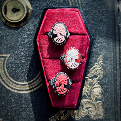 Three cameo rings: a pink skeleton on black, white skeleton on red, and red on a black background.