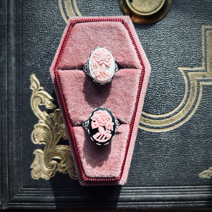Two cameo rings: pink skeletons on white and black backgrounds.