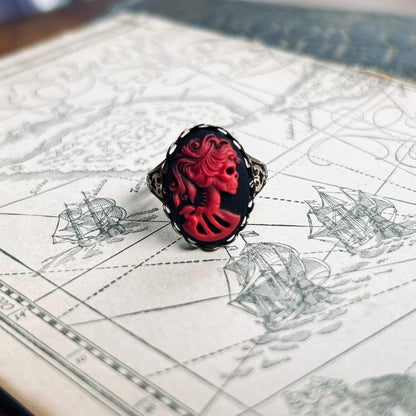 A cameo ring with a red skeleton lady on a black background. This oval cameo is set on an adjustable silver oakleaf ring.