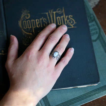 Antiqued silver adjustable filigree ring with white lady profile on a light blue background.
