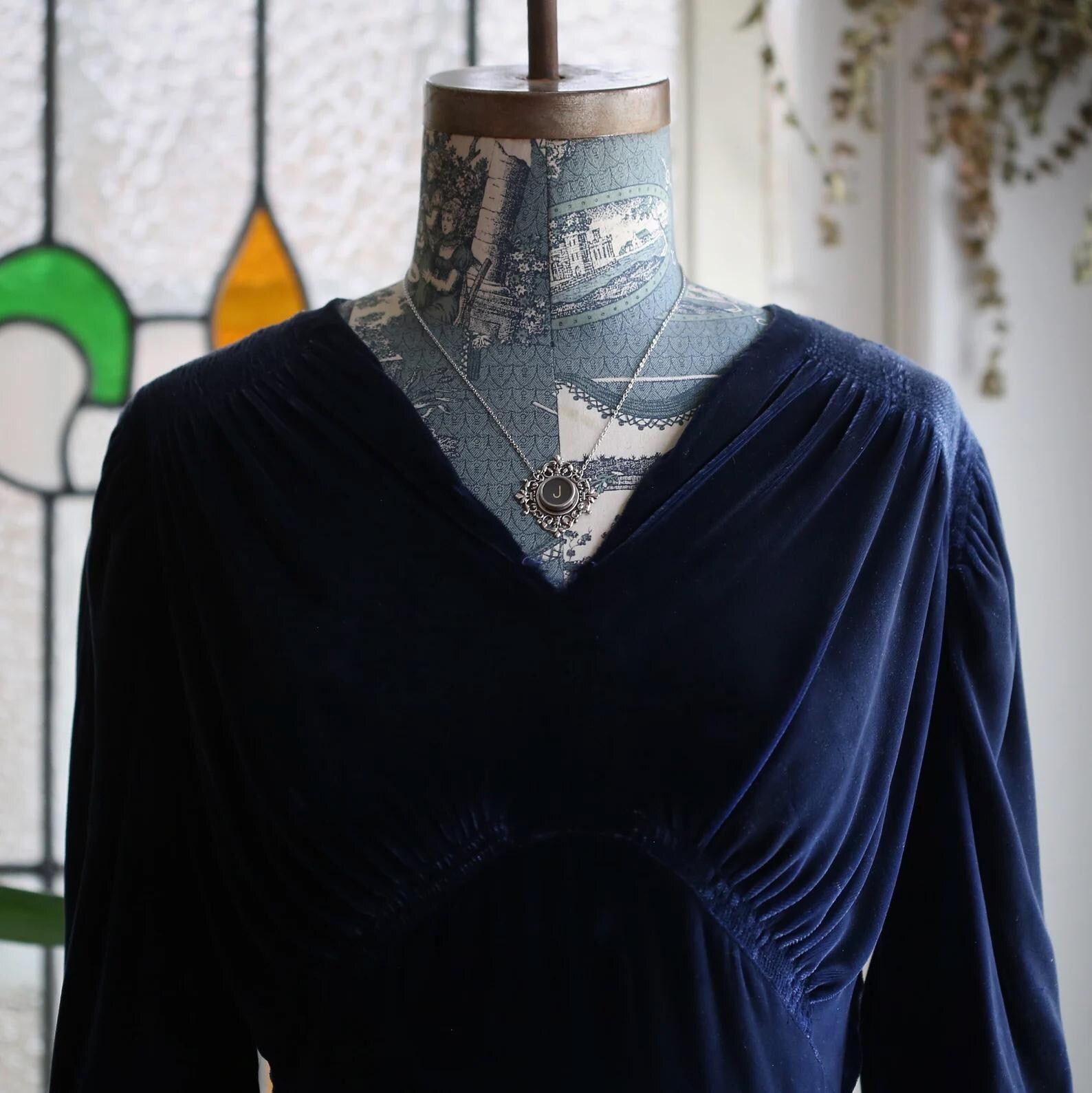 A typewriter key set on a decorative filigree pendant on a necklace chain. Typewriter key is black with a off-white colored letter J.