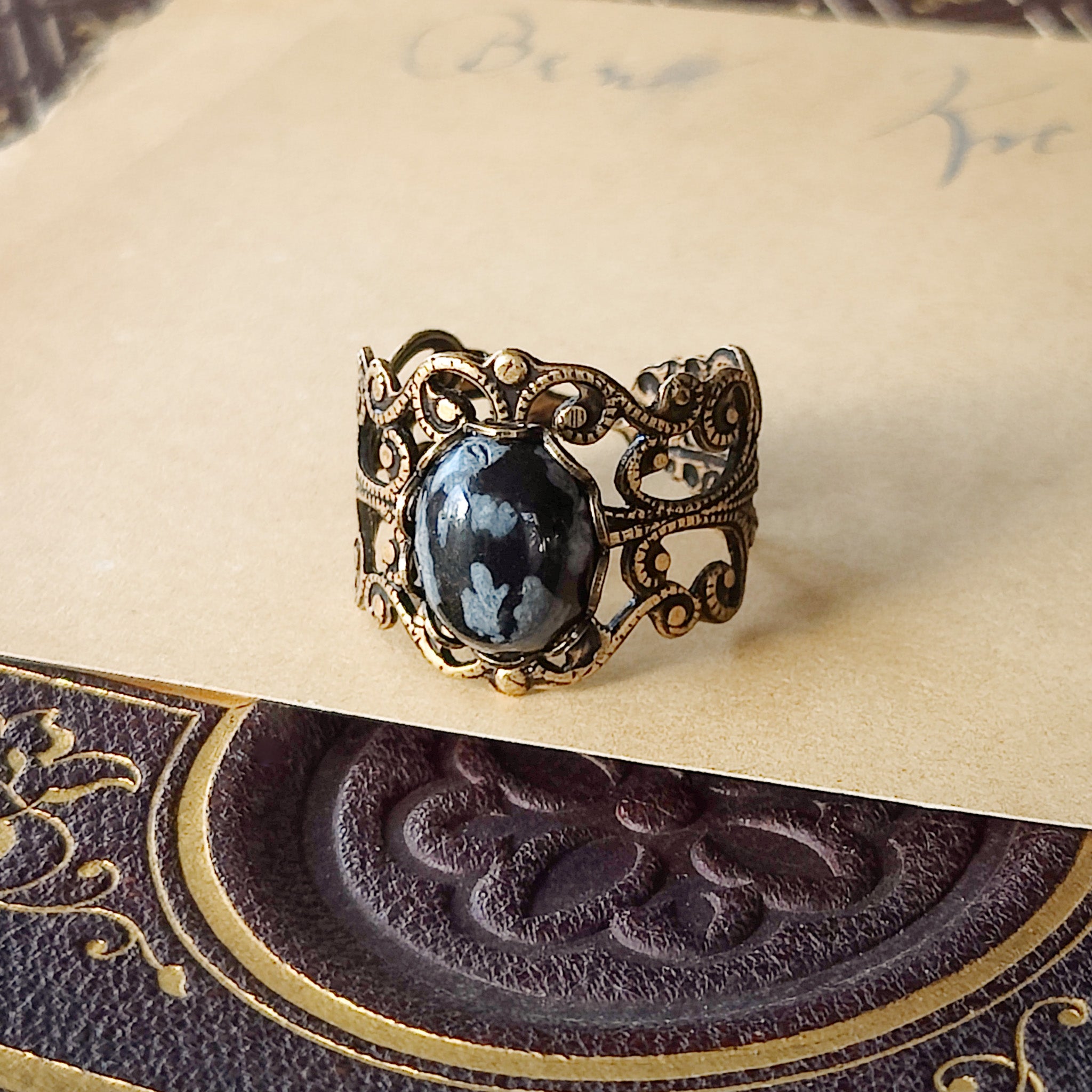 rich antiqued brass modern vintage inspired adjustable filigree ring with a dark black and gray mottled snowflake obsidian oval semi-precious mineral stone set in a military aesthetic
