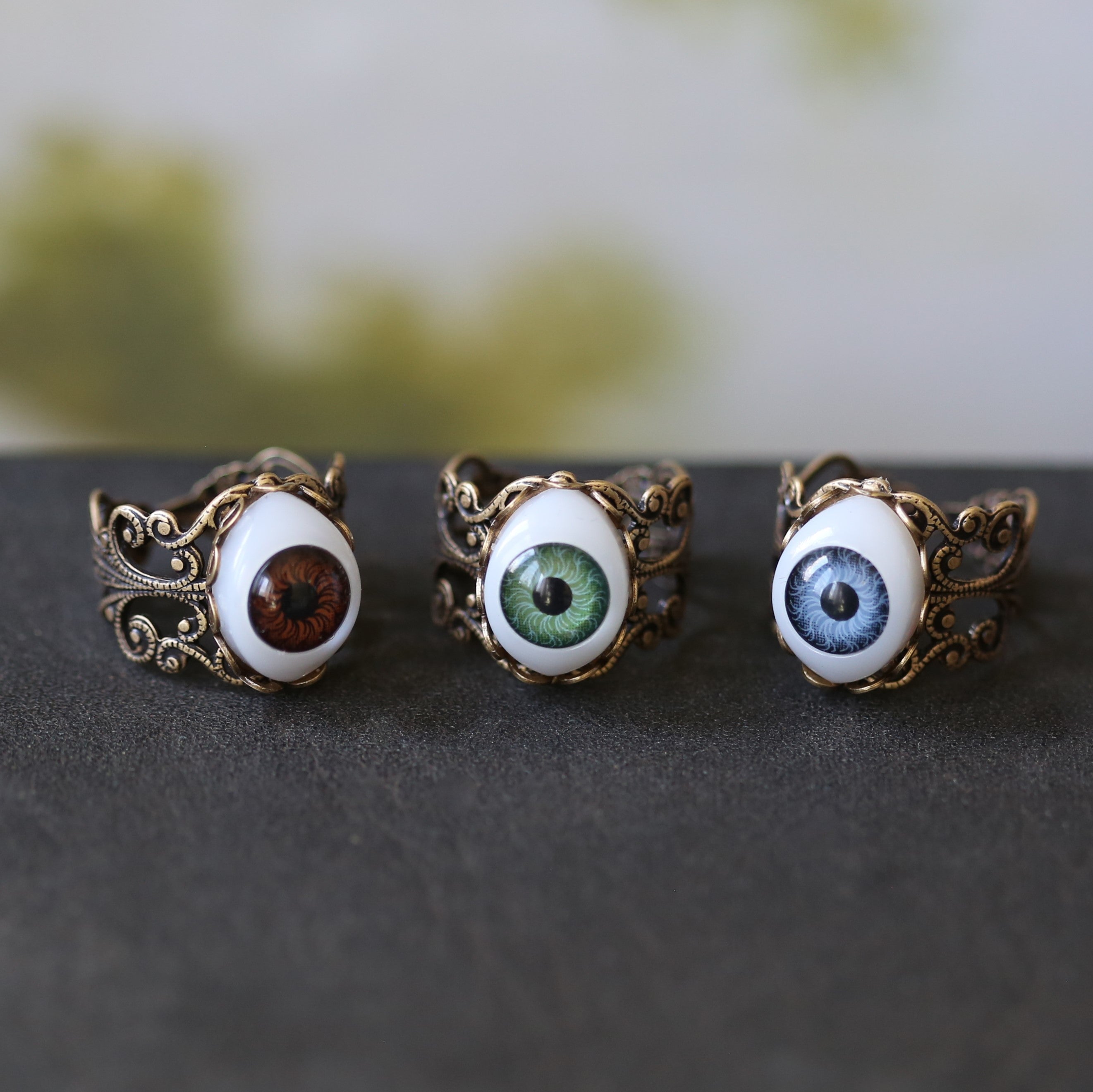 vintage style antiqued brass adjustable filigree ring with a green brown or blue oval evil eye in spooky goblincore style