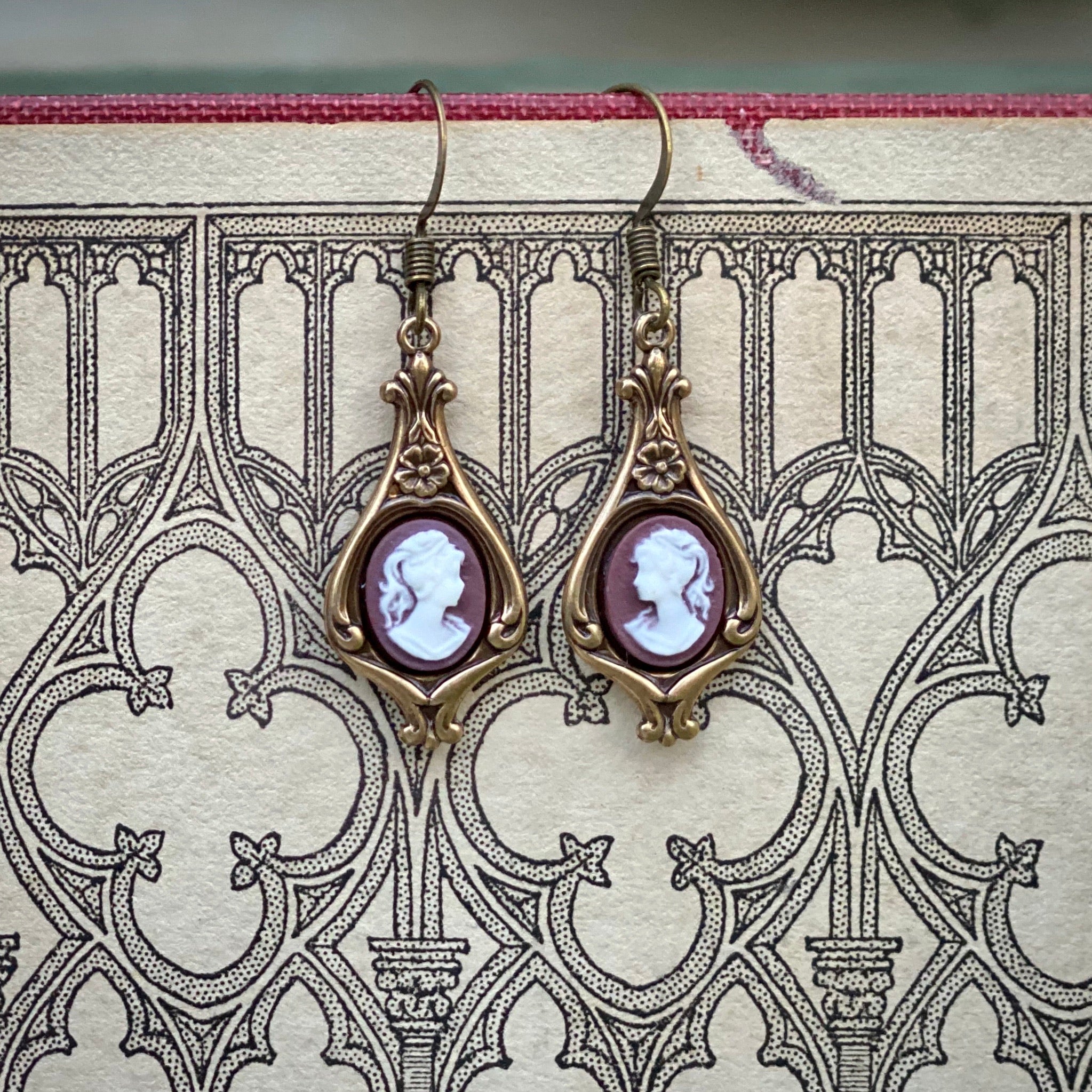 Antiqued brass earrings with purple and white cameos of women on filigree drop settings.